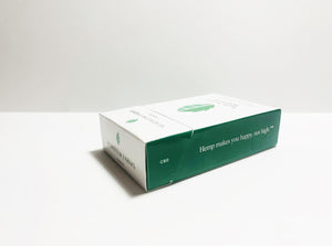 Product displayed resembles a white classic cigarette pack with a large seed/stem logo that is various shades of textured green.  The company logo is on the front flap and the text is in green label with font Manrope.  Pack is shown laying on its back at an angle to display the side tagline which reads, "Hemp makes you happy, not high." along with the acronym, CBD.  The front panel featuring the logo is also visible.  