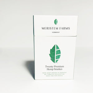 Product displayed resembles a white classic cigarette pack with a large seed/stem logo that is various shades of textured green.  The company logo is on the front flap and the text is in green label with font Manrope.  Pack is viewed from the front on a white background.
